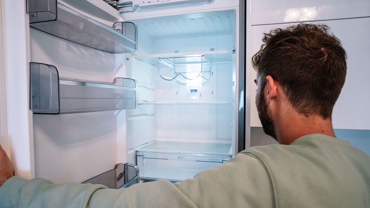 Man looking at empty refrigerator after hosting expensive Thanksgiving dinner and discovering no leftovers remain