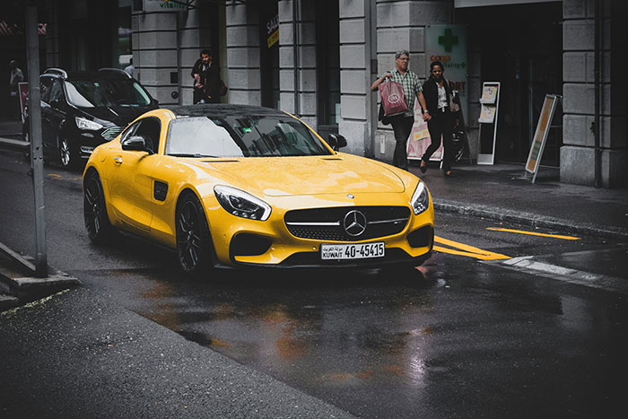 Yellow Mercedes sports car parked on a wet city street with people walking, illustrating people from different countries myths.
