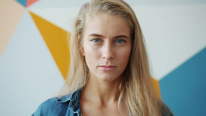 Young woman with long blonde hair and blue eyes against a geometric wall, representing people from different countries.
