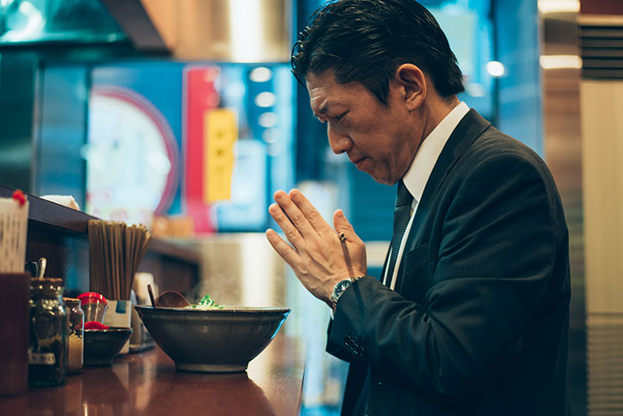 Man from a different country in a suit praying before a bowl of food, denying popular myths foreigners believe.