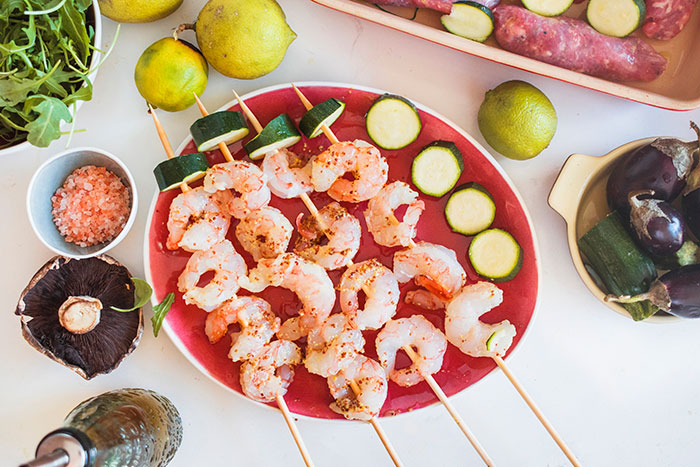 Shrimp skewers with zucchini on a red plate surrounded by fresh vegetables, illustrating people from different countries denying myths.