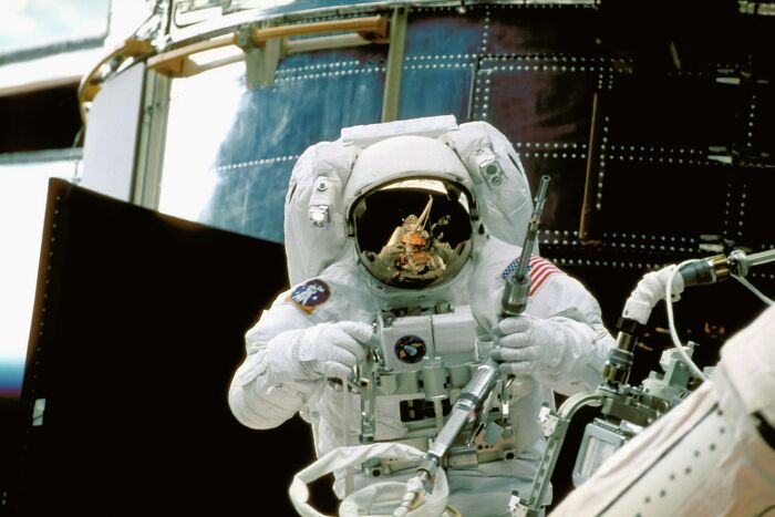 Astronaut performing spacewalk outside spacecraft, showcasing complex equipment in a detailed work of art scene.