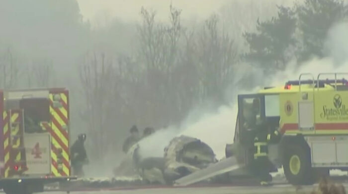 Firefighters spraying water on wreckage at site of plane crash as emergency vehicles respond to the horrific accident.