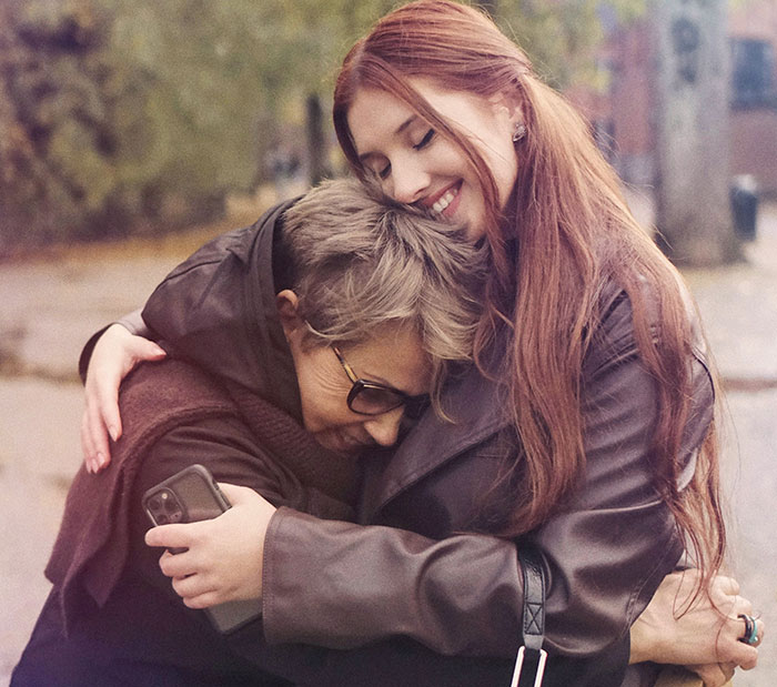 Young woman hugging an older woman outdoors, illustrating a bio mom reacting to daughter honoring dad's bestie as mom at wedding.