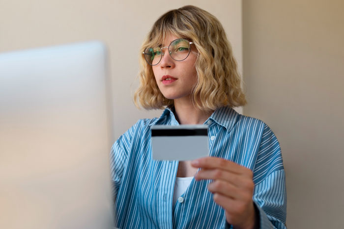 Young woman holding a credit card while looking at a laptop, illustrating karma involving an entitled nephew’s game purchases.