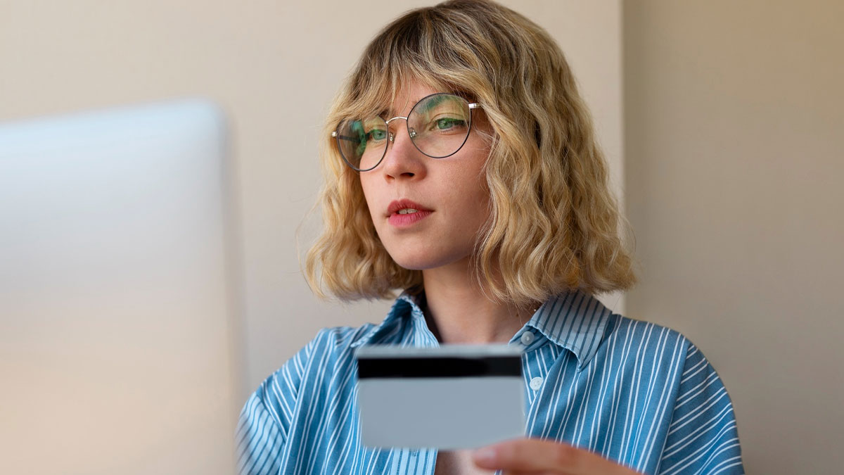 Woman holding a credit card and looking at a laptop, illustrating karma for an entitled nephew using the card for games