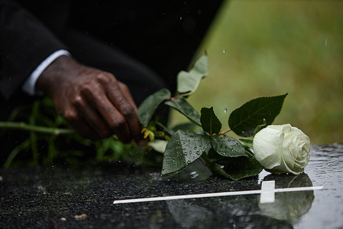 Hand placing a white rose on a gravestone, symbolizing loss and family conflict after father's estrangement from late wife's family. Hand placing a white rose on a gravestone, symbolizing loss and family conflict after father's estrangement from late wife's family.