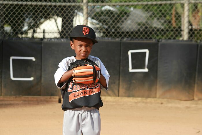 Young baseball player wearing Giants cap and glove on field, capturing a moment from true stories that sound made up.