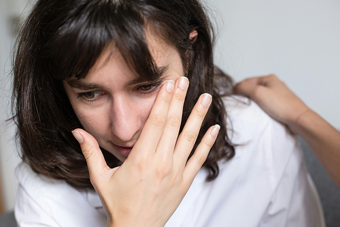 Young woman showing embarrassment, covering face with hand while a comforting hand rests on her shoulder. Young woman showing embarrassment, covering face with hand while a comforting hand rests on her shoulder.
