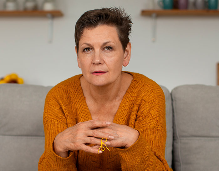 Middle-aged woman in an orange sweater sitting on a couch, looking thoughtful about no vegan options Christmas Eve dinner. Middle-aged woman in an orange sweater sitting on a couch, looking thoughtful about no vegan options Christmas Eve dinner.