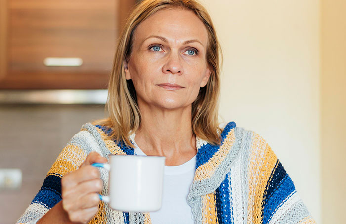Middle-aged woman in a knitted sweater holding a white mug, reflecting on no vegan options Christmas Eve dinner challenges. Middle-aged woman in a knitted sweater holding a white mug, reflecting on no vegan options Christmas Eve dinner challenges.