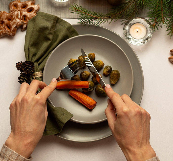 Hands cutting roasted carrots and Brussels sprouts on a plate, illustrating no vegan options Christmas Eve dinner setting. Hands cutting roasted carrots and Brussels sprouts on a plate, illustrating no vegan options Christmas Eve dinner setting.