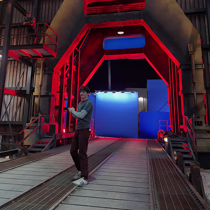 Noah Schnapp recreates a Stranger Things scene on set with red lighting and blue screen background at night.