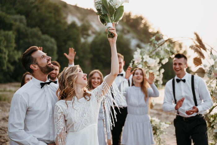Bride smiling and holding up bouquet after catching it during outdoor wedding ceremony with joyful guests around. Bride smiling and holding up bouquet after catching it during outdoor wedding ceremony with joyful guests around.