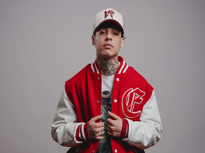 Young man in a red and white varsity jacket and cap, showing signs of being stuck in his high school era style.