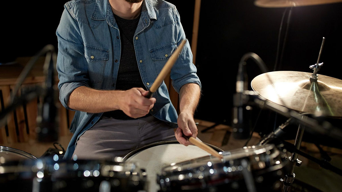 Man playing drums in a studio, wearing a denim shirt, highlighting once famous regular job in music performance.