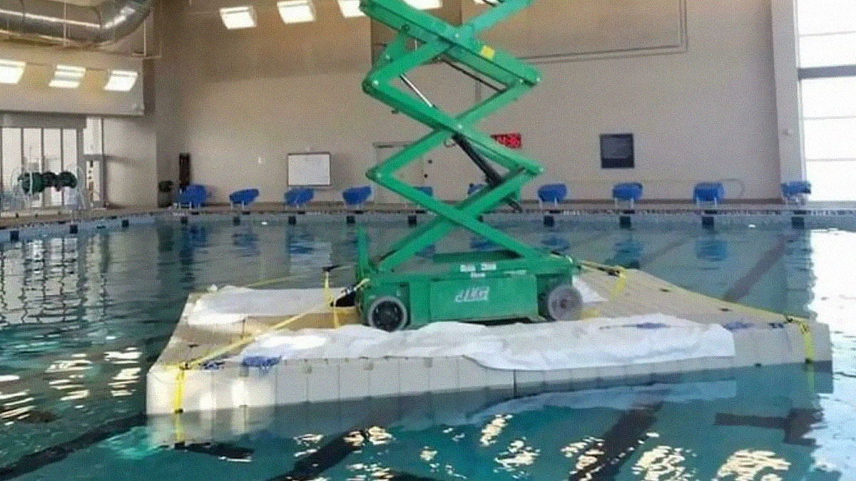 Green scissor lift placed on a floating platform in a pool, showcasing employees blatantly ignoring safety protocol hazards.