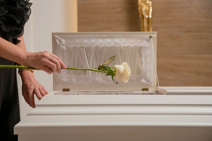 Person placing a white rose inside a coffin during a funeral, capturing a poignant life fact moment.