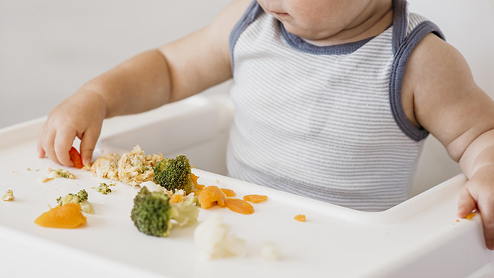 Five-month-old baby sitting in a high chair with scattered baby food, highlighting risks of pseudoscience parenting choices. Five-month-old baby sitting in a high chair with scattered baby food, highlighting risks of pseudoscience parenting choices.