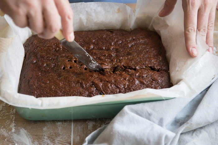 Hands cutting a freshly baked chocolate cake in a pan with parchment paper, illustrating parents lied about allergies concept. Hands cutting a freshly baked chocolate cake in a pan with parchment paper, illustrating parents lied about allergies concept.