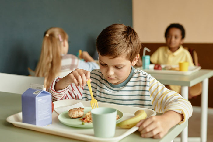 Young boy eating lunch at school cafeteria, highlighting issues with parents lied about allergies concerns. Young boy eating lunch at school cafeteria, highlighting issues with parents lied about allergies concerns.