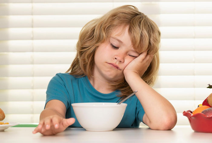 Child looking bored and resting head on hand while sitting at table with empty bowl, representing parents lied about allergies impact. Child looking bored and resting head on hand while sitting at table with empty bowl, representing parents lied about allergies impact.