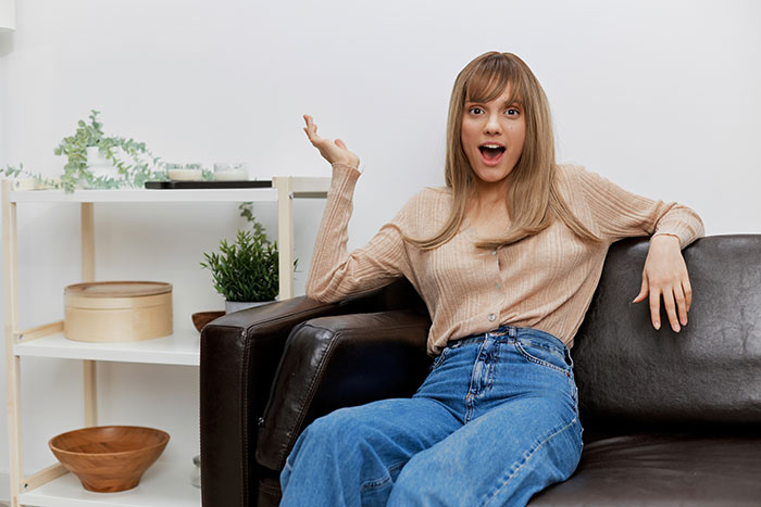Young woman with surprised expression sitting on a couch, illustrating moments parents realized their kids are monsters.
