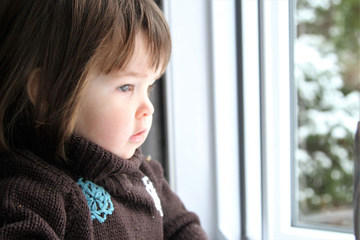 Young child looking out a window with a serious expression, illustrating moments parents realize kids can be selfish or unloving.
