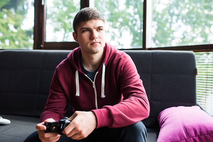 Teenage boy with a game controller sitting on a couch, portraying a vain and selfish unloving sociopath moment.