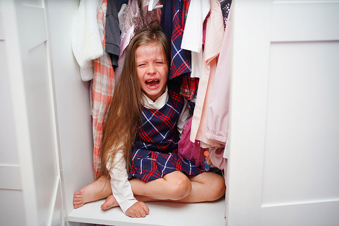 Crying young girl sitting in a closet, illustrating a vain selfish unloving sociopath behavior in children.