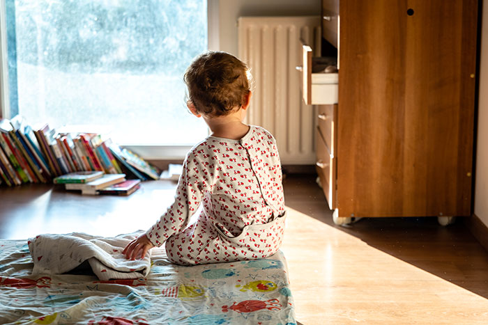 Toddler sitting on a blanket in a sunlit room, with a bookshelf and wooden furniture nearby, illustrating kids as monsters.