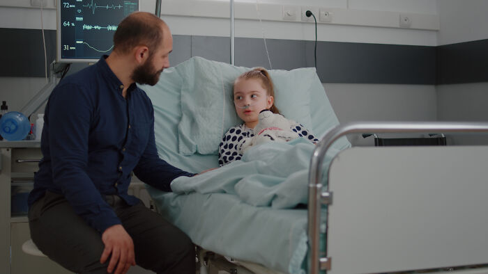 Man sitting beside hospital bed talking to young girl, illustrating stories of people sharing the fastest they quit a job.
