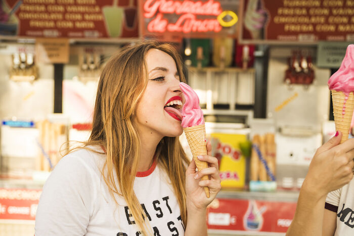 Young woman enjoying pink ice cream cone at a vibrant ice cream stand, illustrating quick job quitting stories shared by people.