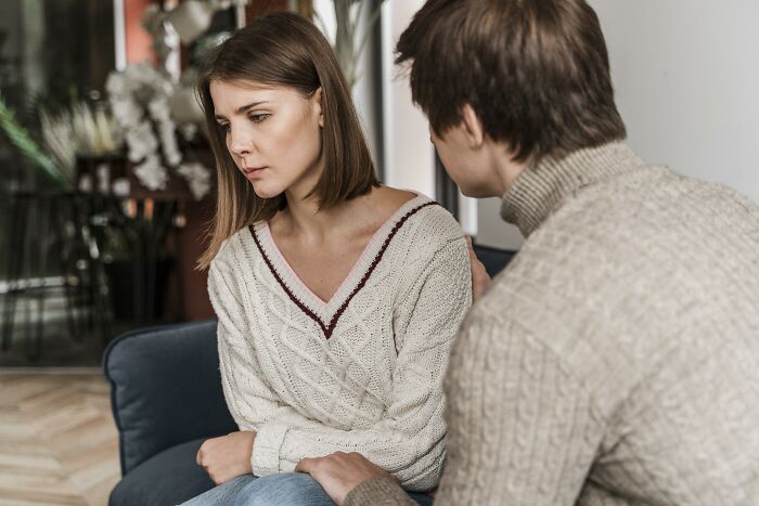 Couple having serious conversation at home, woman looking upset as man tries to comfort her in tense moment.