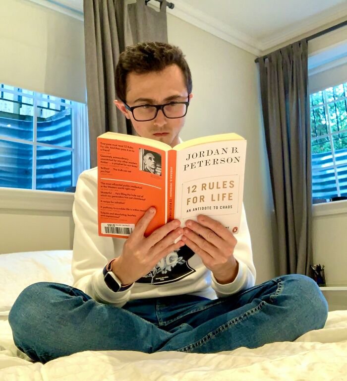 Young man wearing glasses reading Jordan B. Peterson's 12 Rules for Life book, reflecting on terrifying partner secrets.
