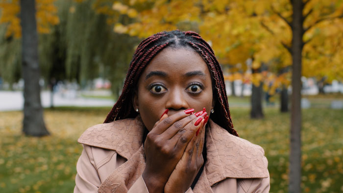 Woman with braided hair covering her mouth in shock, expressing fear outdoors, representing scariest moments that left trauma.