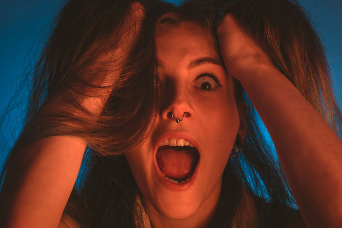 Young woman with a nose ring screaming and holding her hair, depicting trauma from scariest moments shared by people.