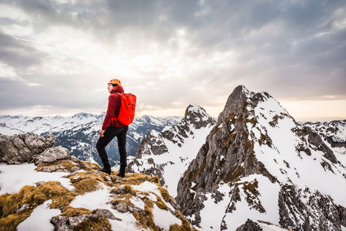 Hiker standing on snowy mountain edge facing rugged peaks, evoking scary moments that left them traumatized.
