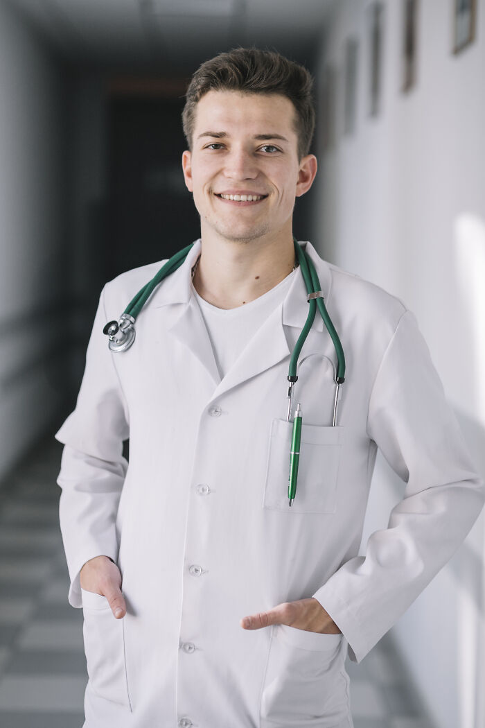 Young male doctor smiling confidently in hospital hallway with stethoscope showing how doctors have truly heard everything.