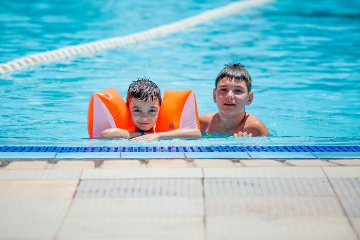 Two boys in a swimming pool, one with orange floaties, captured in a moment that feels scary and unforgettable.
