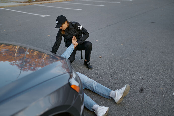 Police officer helping injured person lying on asphalt near parked car, capturing a scary moment still talked about today