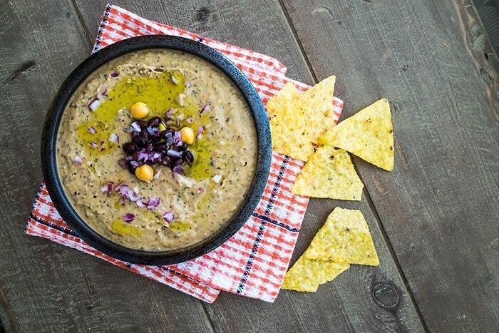 Bowl of hummus topped with chickpeas and olives served with tortilla chips, a dish foodies say didn’t need a gourmet upgrade.