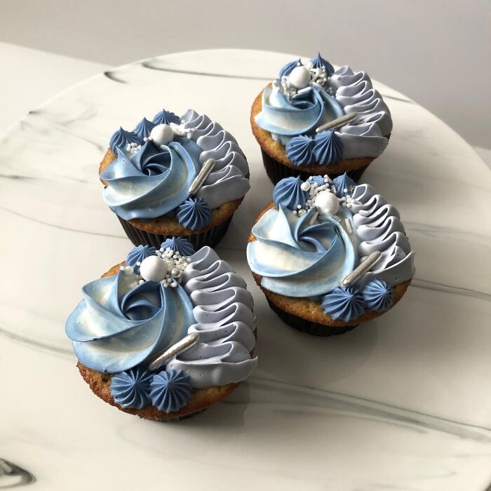 Four cupcakes with blue and white decorative frosting and edible pearls, showcasing dishes foodies say didn’t need gourmet upgrades.