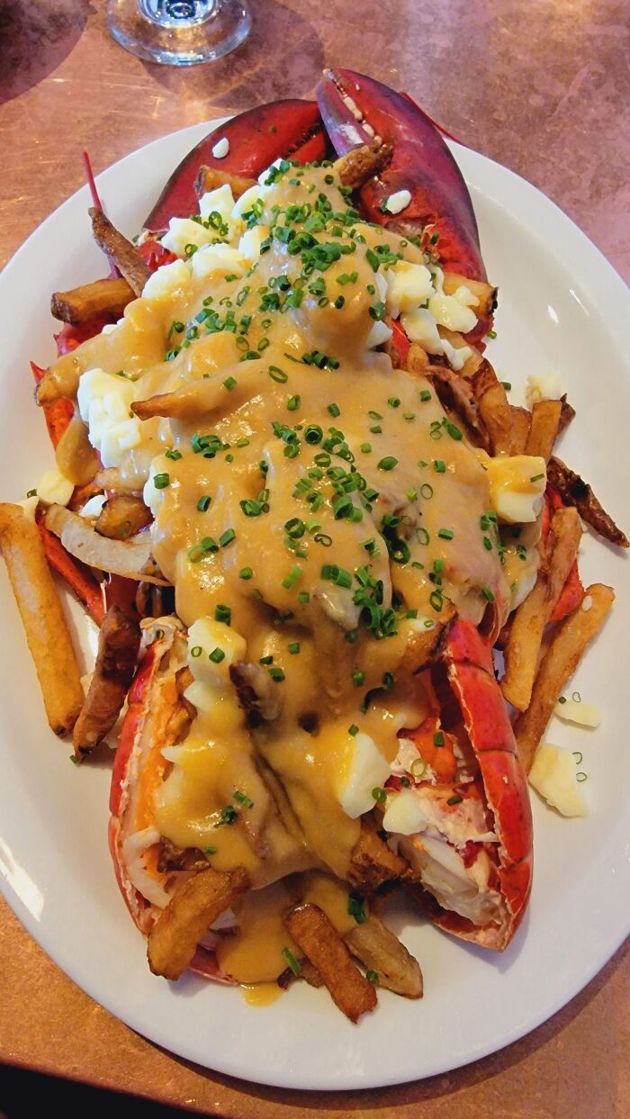 Lobster poutine with cheese curds, gravy, and fries on a white plate at a casual dining setting.
