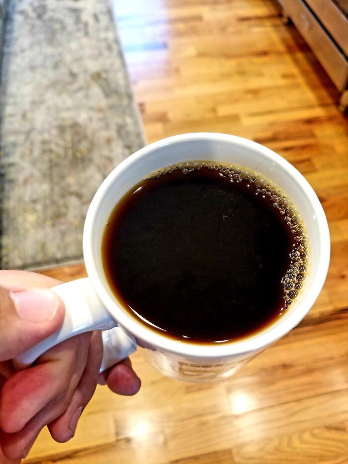 Hand holding a white mug filled with black coffee, showcasing a simple dish foodies say didn’t need a gourmet upgrade.