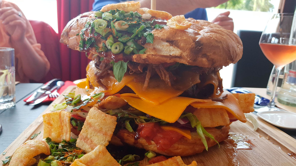 Close-up of a loaded sandwich with cheddar, pulled meat, and fresh herbs, a dish foodies say didnu2019t need a gourmet upgrade.