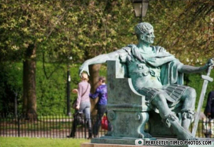 Bronze statue of a Roman soldier with people walking in the background, a perfectly timed photo capturing stillness and motion.