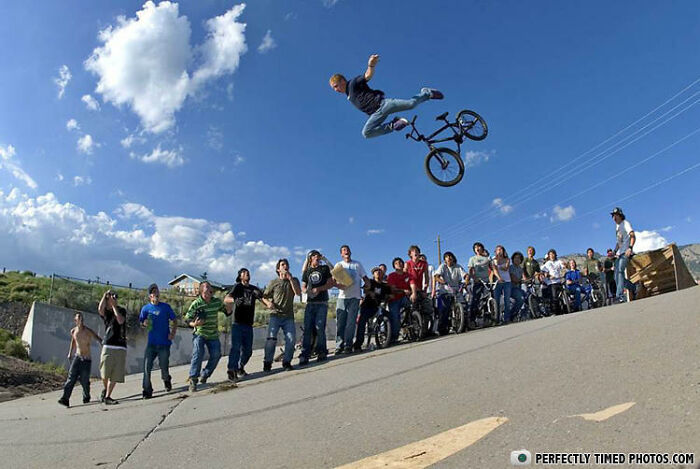 BMX rider performing a stunt mid-air with a crowd watching on a sunny day, a perfectly timed photo capturing the moment.