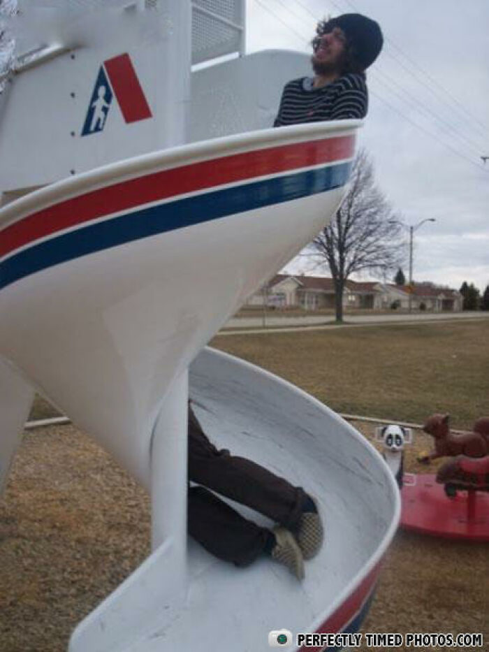 Person smiling at top of playground slide while another person is stuck halfway down in a perfectly timed photo.