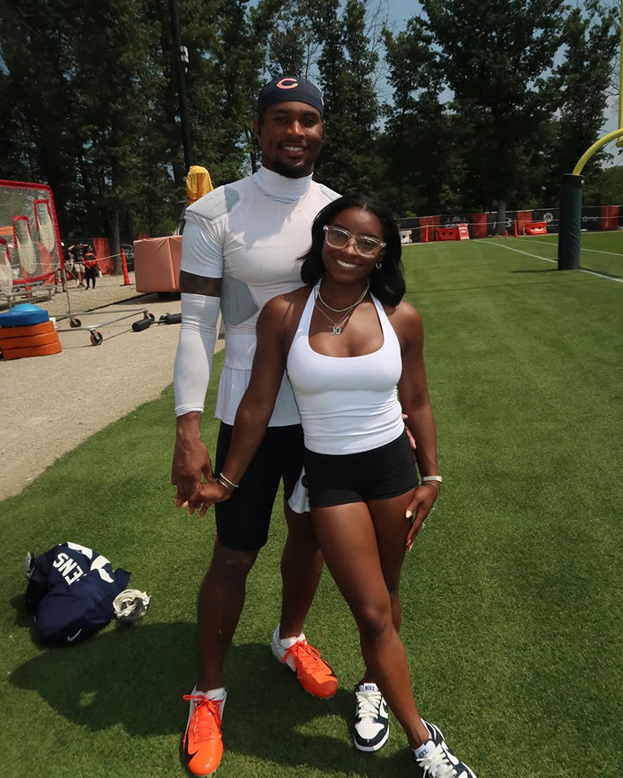 Simone Biles smiling outdoors on a sports field, wearing athletic attire and standing with a man in sporty clothes. Simone Biles smiling outdoors on a sports field, wearing athletic attire and standing with a man in sporty clothes.